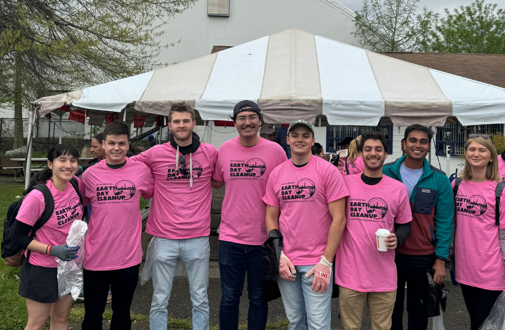 A group of men and women, smiling at the camera and standing together outside. They are wearing pink shirts which read: "Earth Day Cleanup."