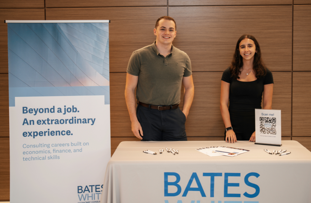 A young man and woman stand behind a recruiting table. Beside them, a banner reads: "Beyond a job. An extraordinary experience." The Bates White logo is at the bottom of the sign.