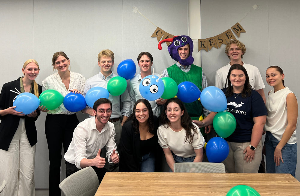 A group of young men and women smiling together. Many are holding balloons that have been tied together to make an animal.