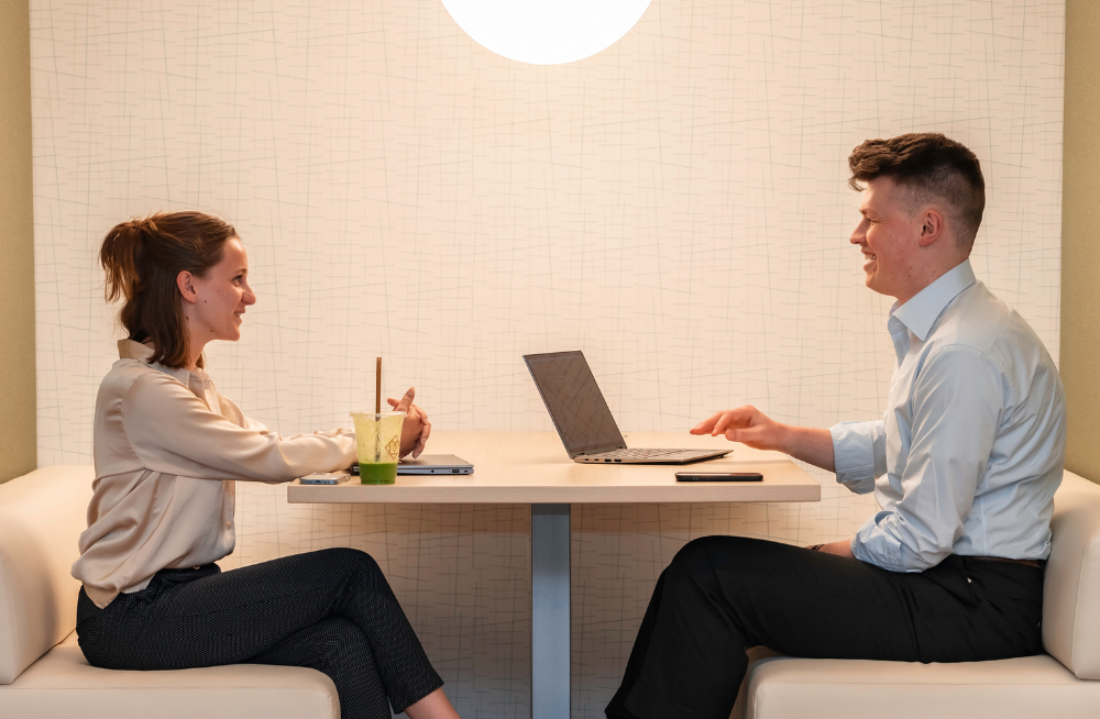 A young man and woman sit across from each other at a table, in the middle of a conversation.