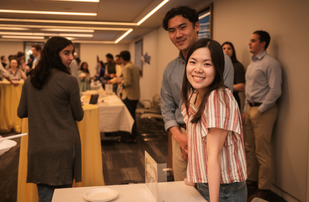 A young man and woman standing behind a table station, smiling at the camera.