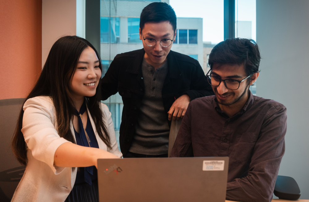 One young woman and two young men are gathered around a computer.