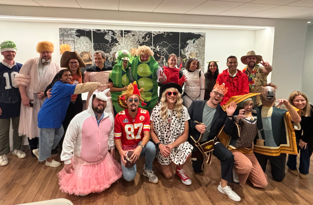 A group of 19 people are gathered together (standing and kneeling) and smiling at the camera. They are dressed in different costumes.